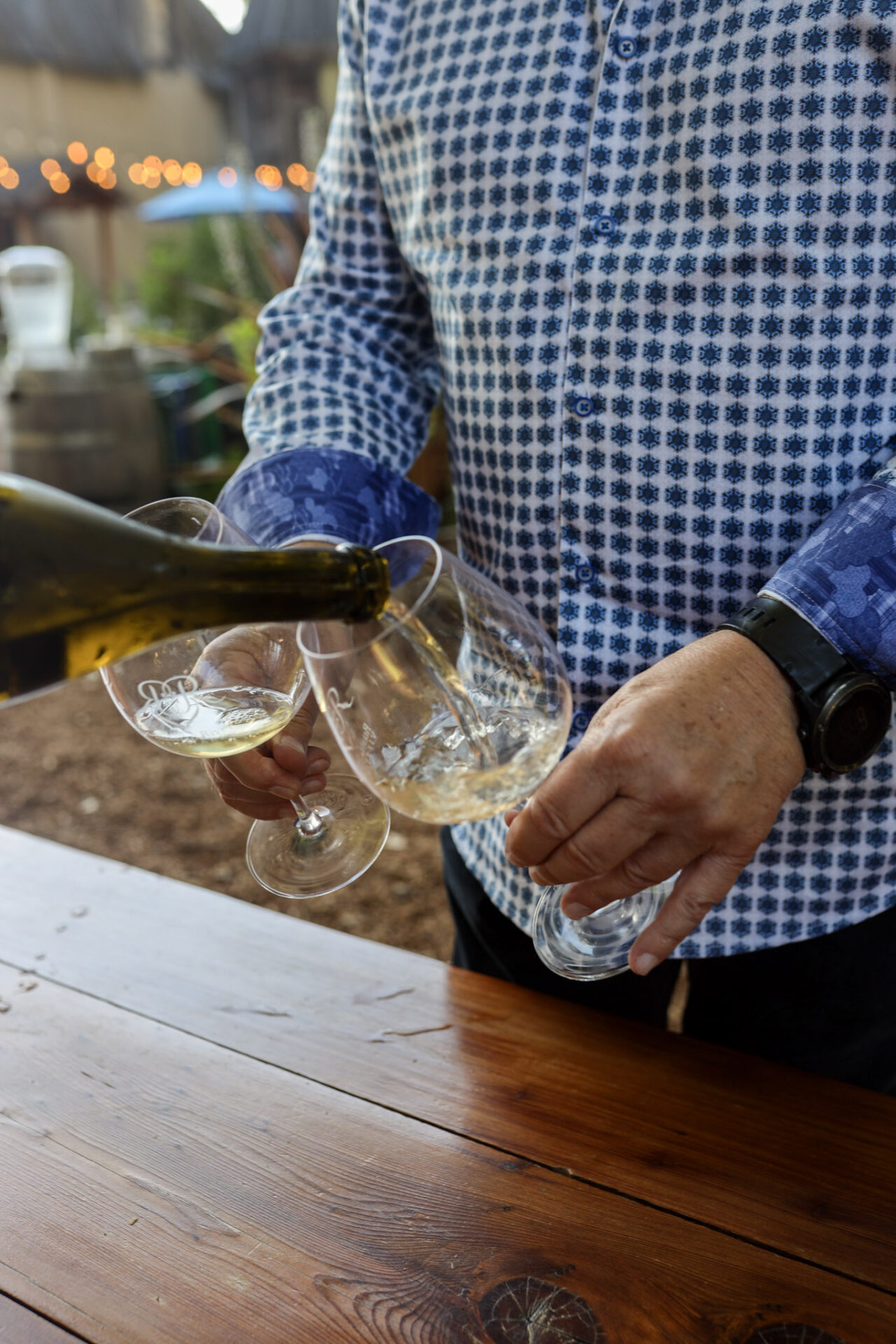 A man's hands holding two glasses while someone pours white wine