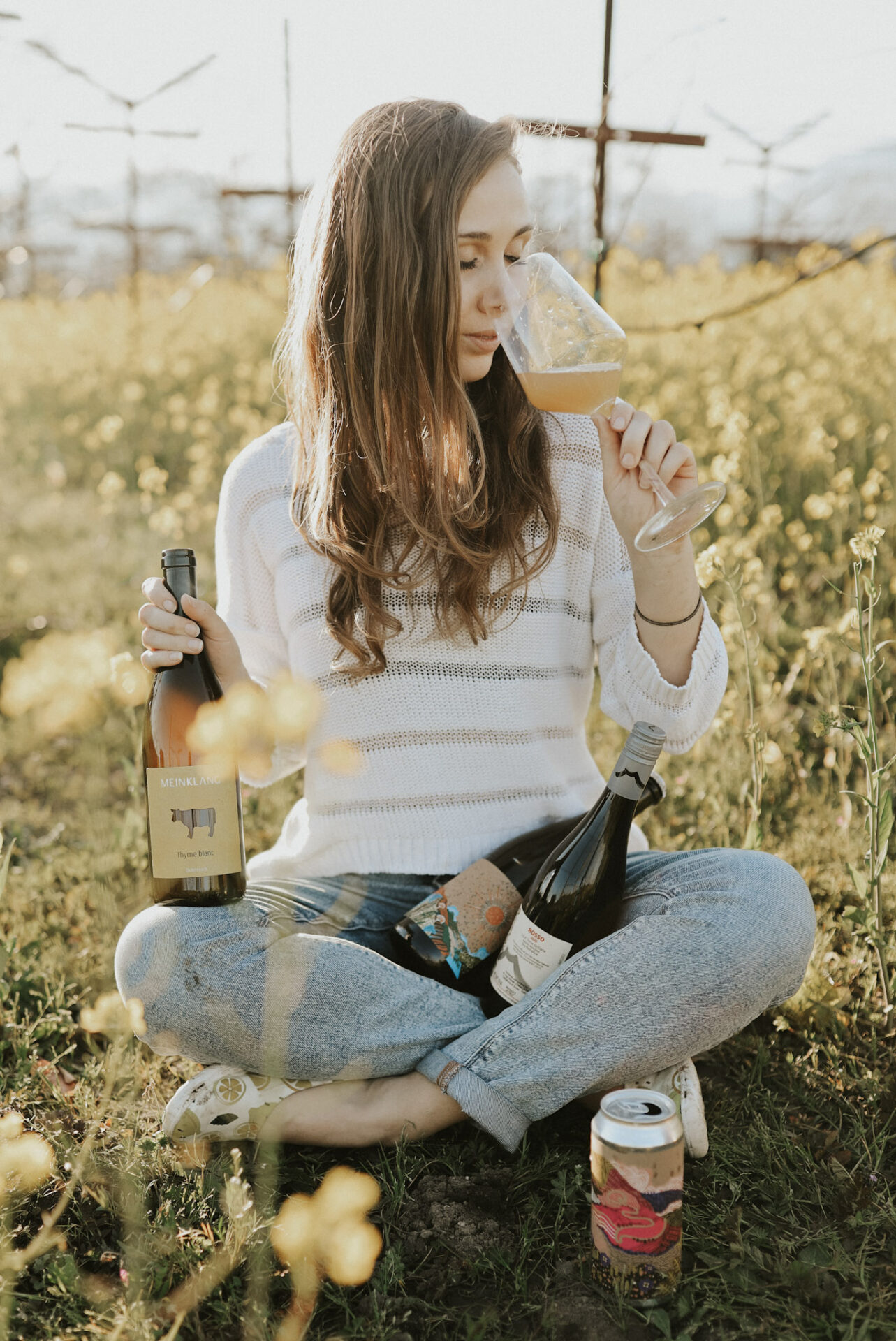 Paige in a field of yellow flowers sipping Pinot Grigio