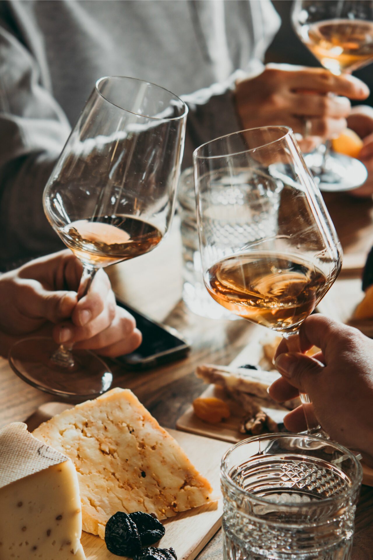 Wine glasses cheersing with food and cellphone in background