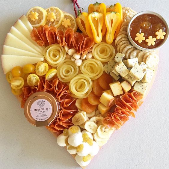 yellow inspired heart shaped charcuterie board with cheese, meats, and vegetables