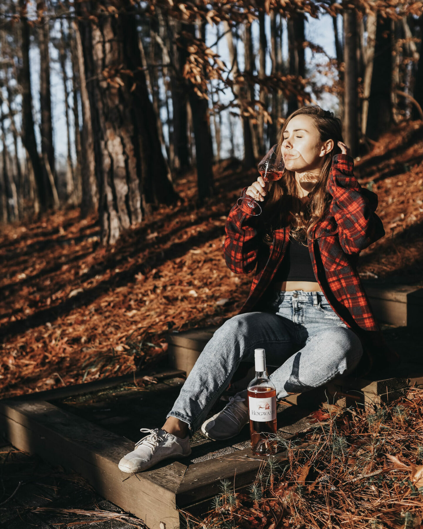 Paige drinking Hogwash rose wine outside in a rustic setting, wearing plaid