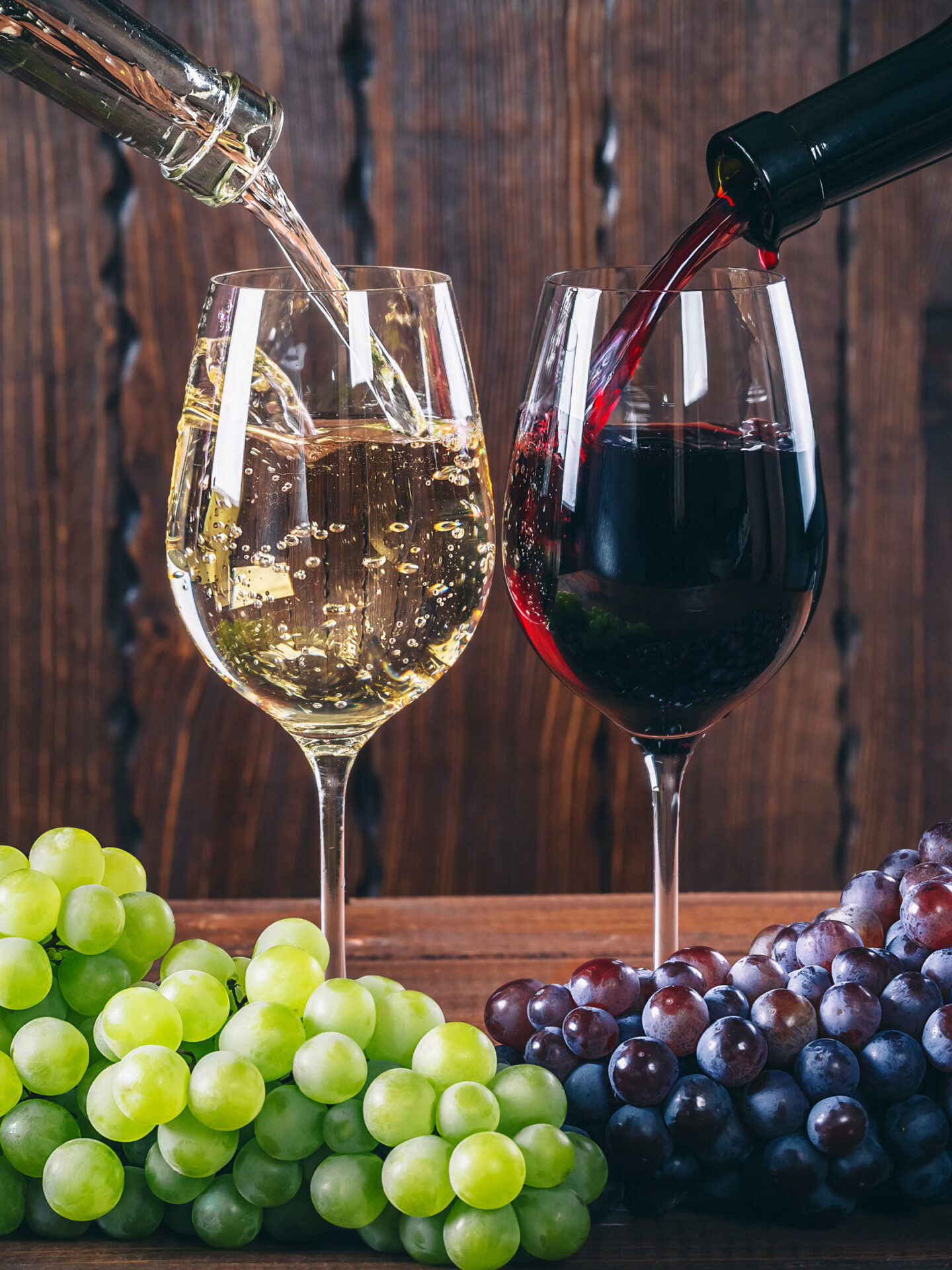 Pinot Grigio vs Pinot Noir in wine glasses with wine grapes on table