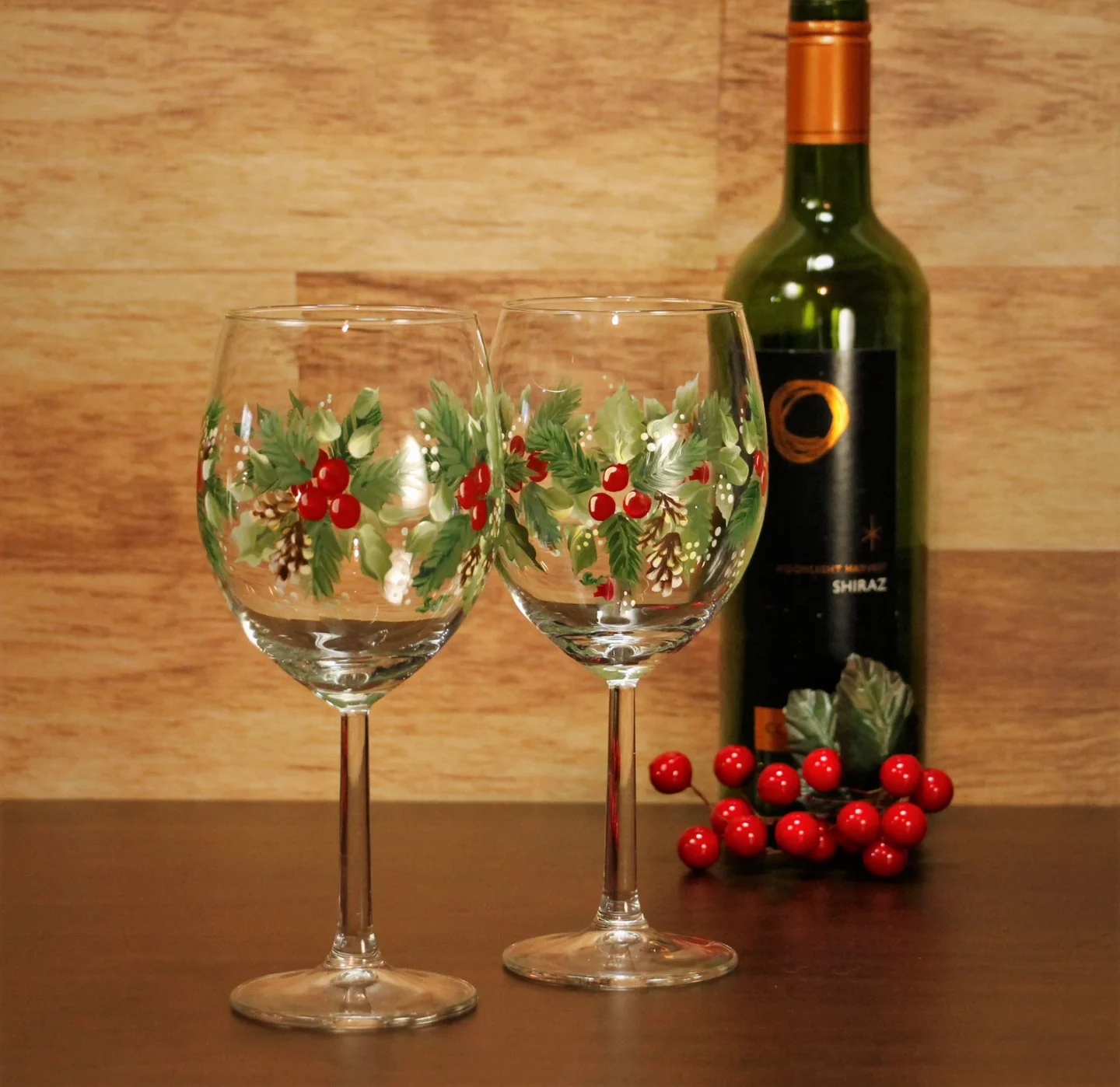 Two hand painted, stemmed wine glasses featuring Christmas holly
