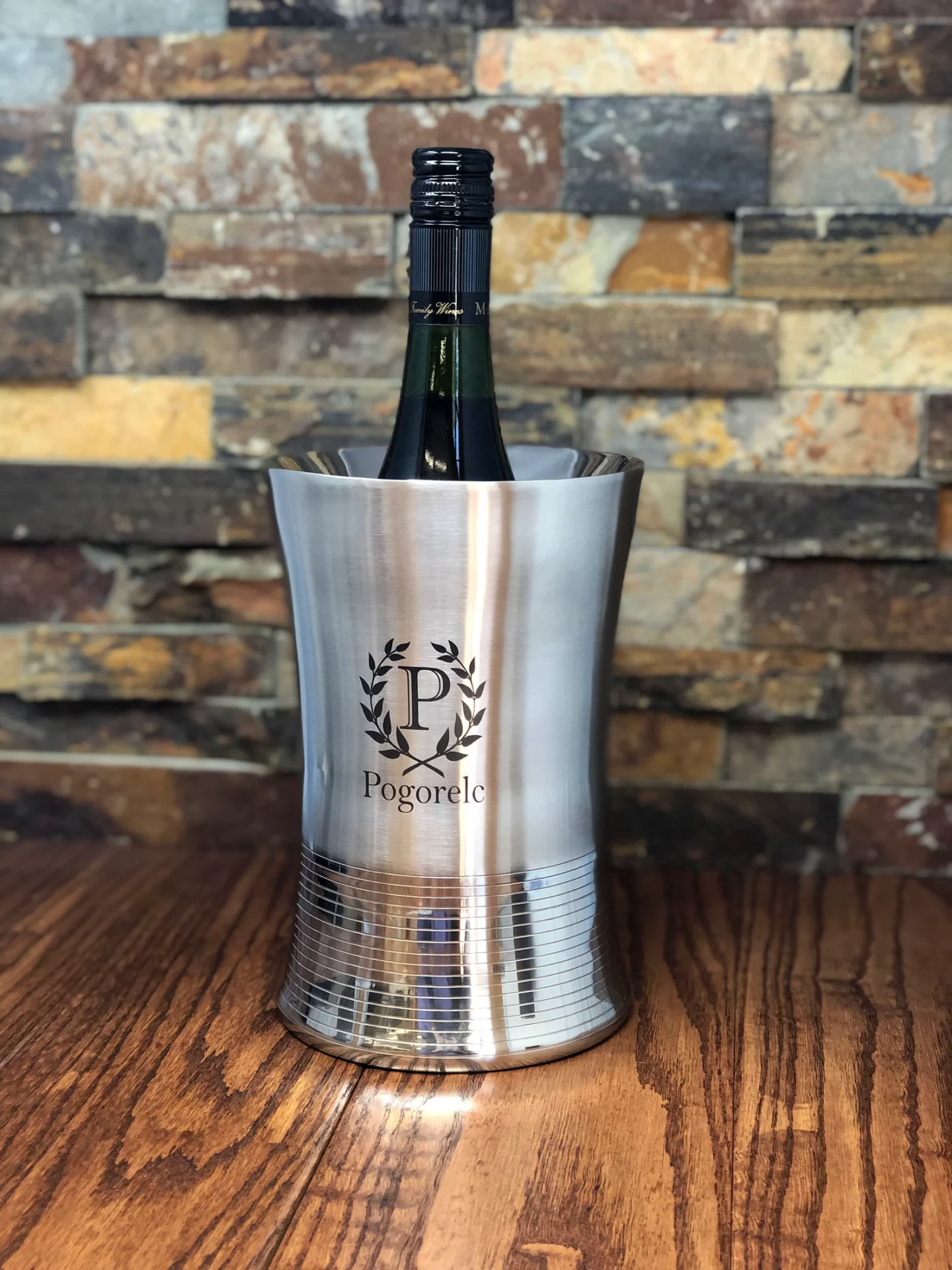 Stainless steel wine chiller holding a bottle of wine on a wooded table top and stone background