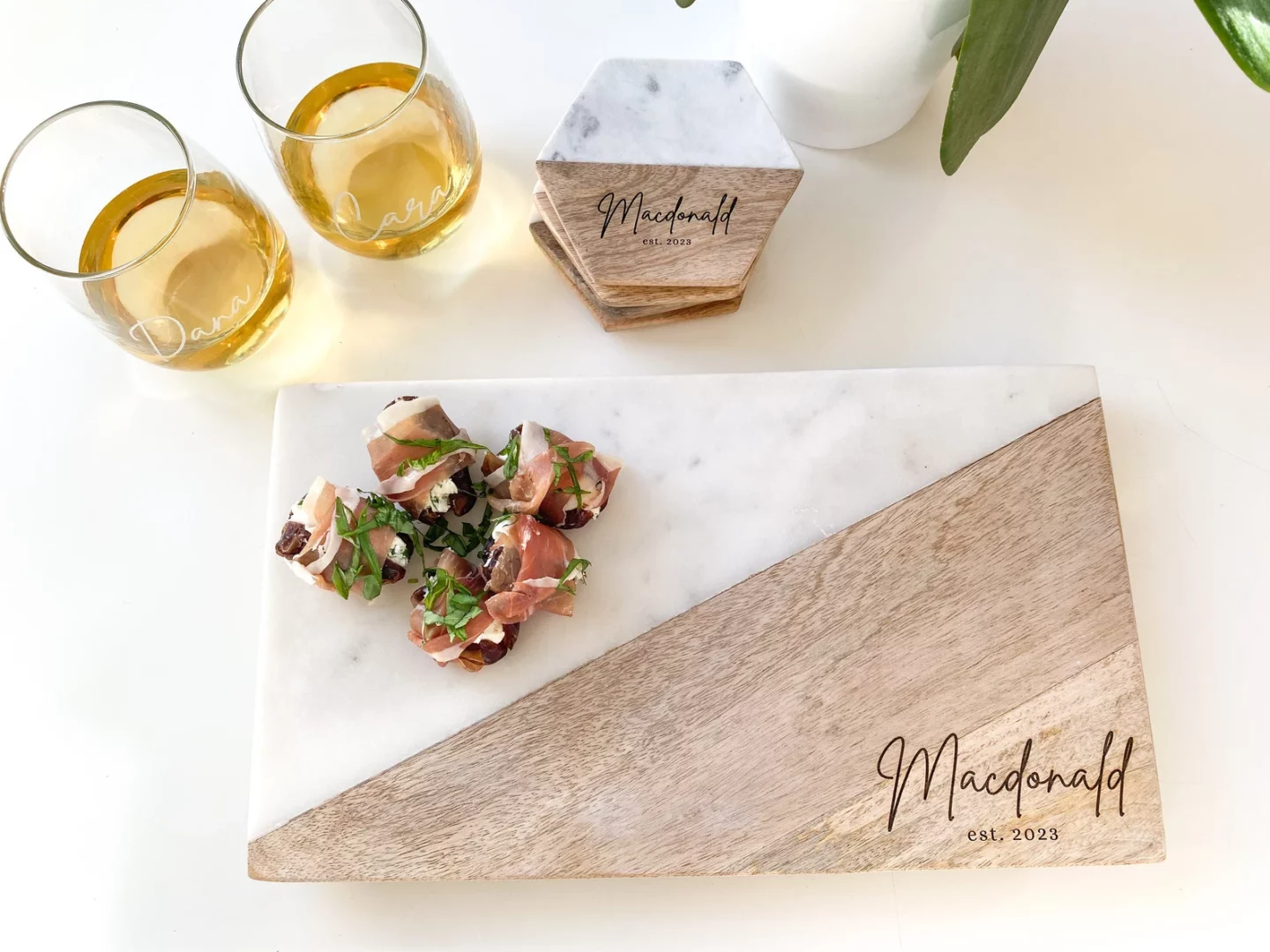 Meat and cheese plated on a marble and wood charcuterie board beside matching coasters and wine glasses