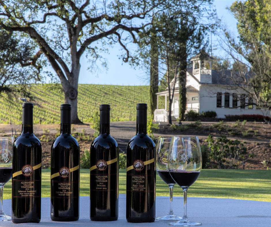 Four bottles of wine pictured in front of rolling vineyard hills and church