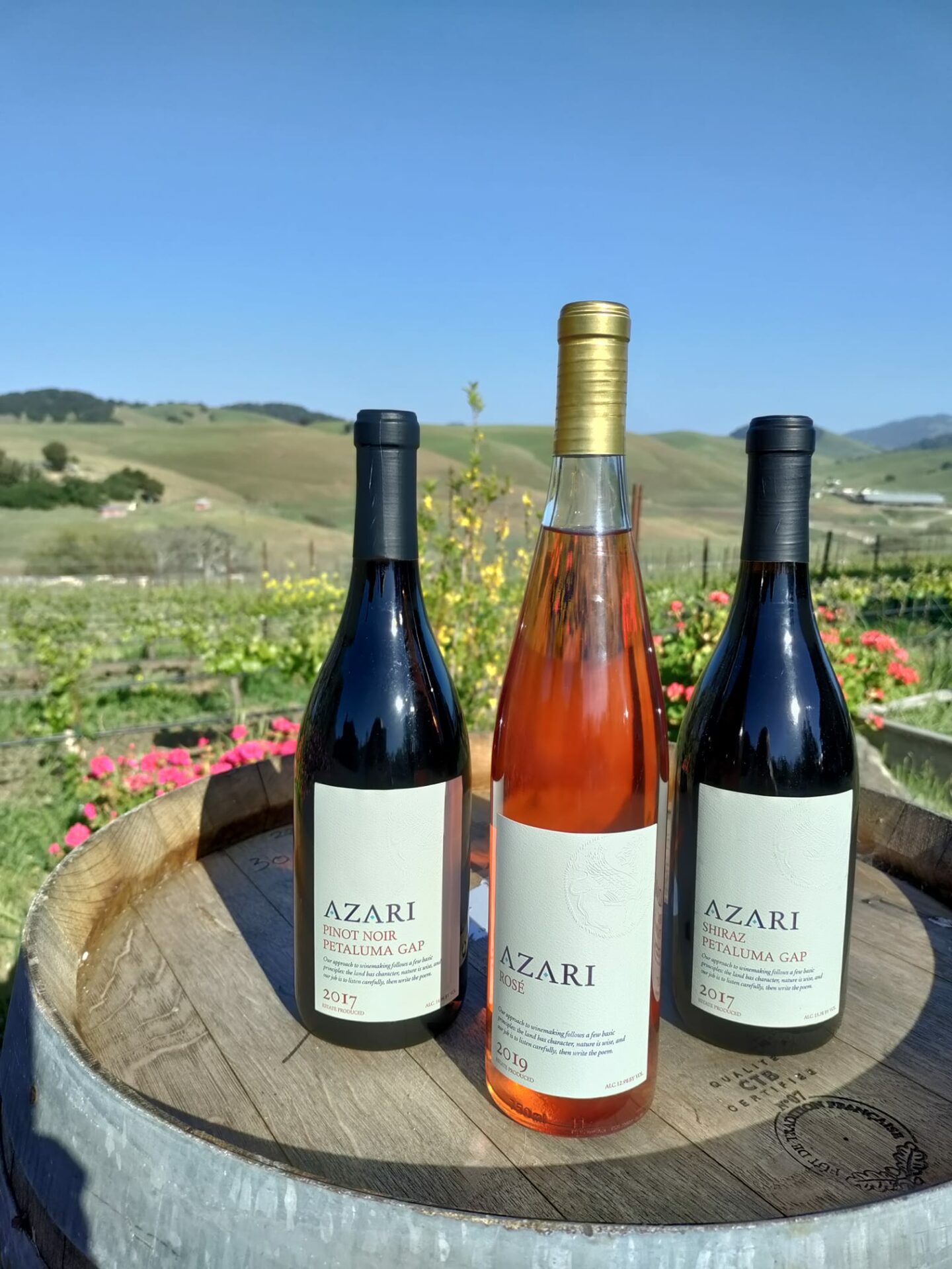 A bottle of Pinot Noir, Rose, and Shiraz placed on top of an oak barrel