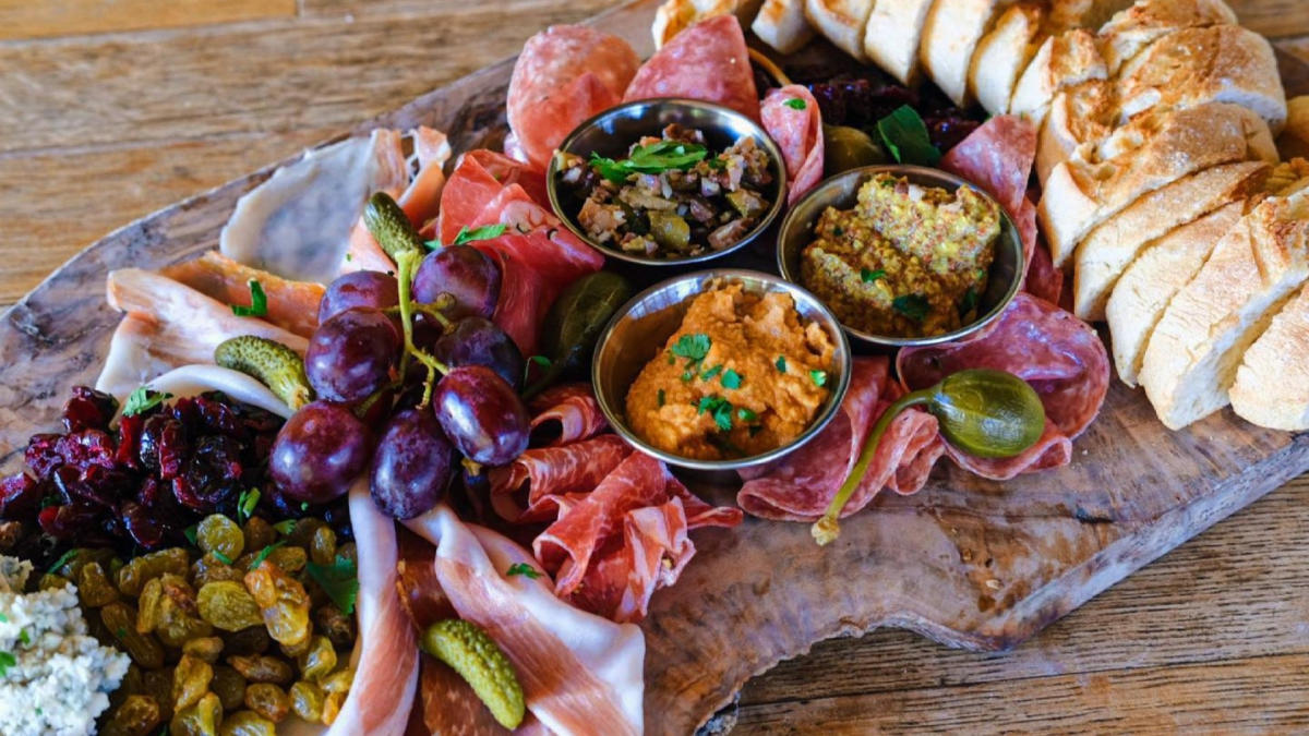 Charcuterie board and dipping sauces plated with breads, meats, and cheeses