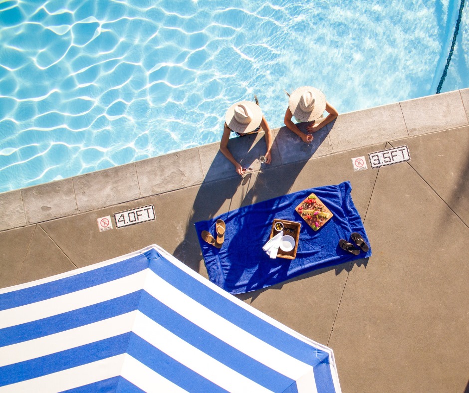 Two women enjoy wines and food by the poolside