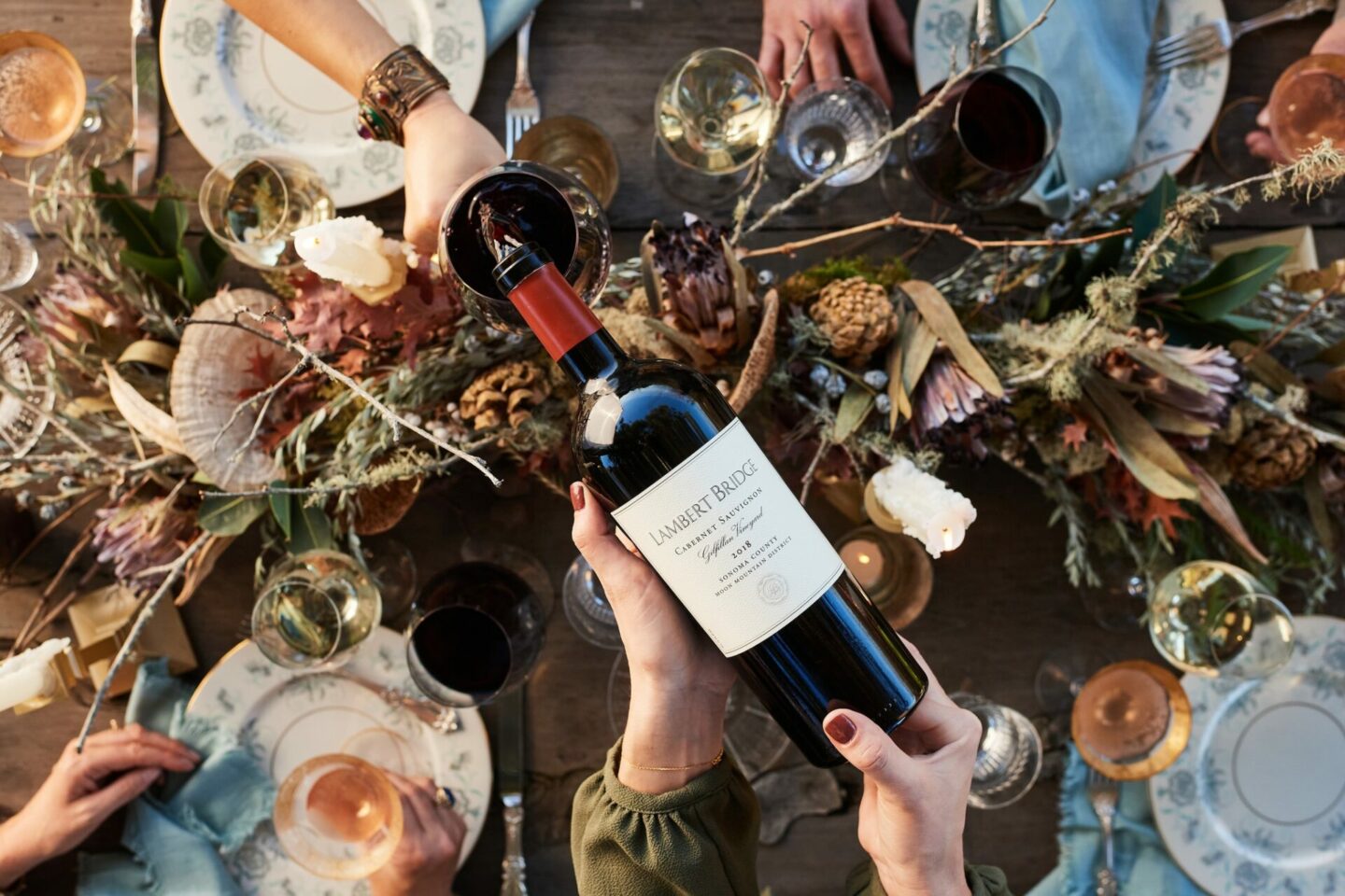 A hand pours a glass of Cabernet Sauvignon over a decorative table