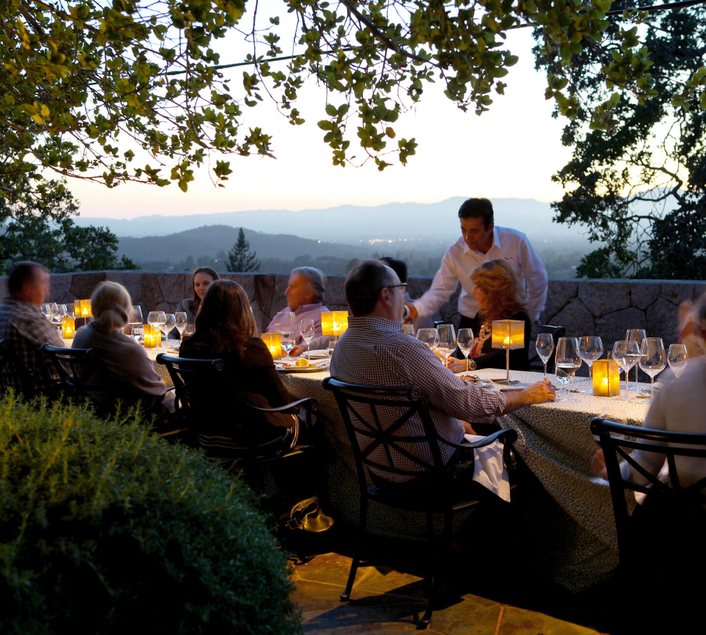 People seated around a long dinning table and being served wine overlooking the Coombsville Ava