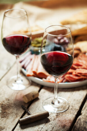 Two glasses of Cabernet Pfeffer wine on a wooden table with charcuterie meats in background