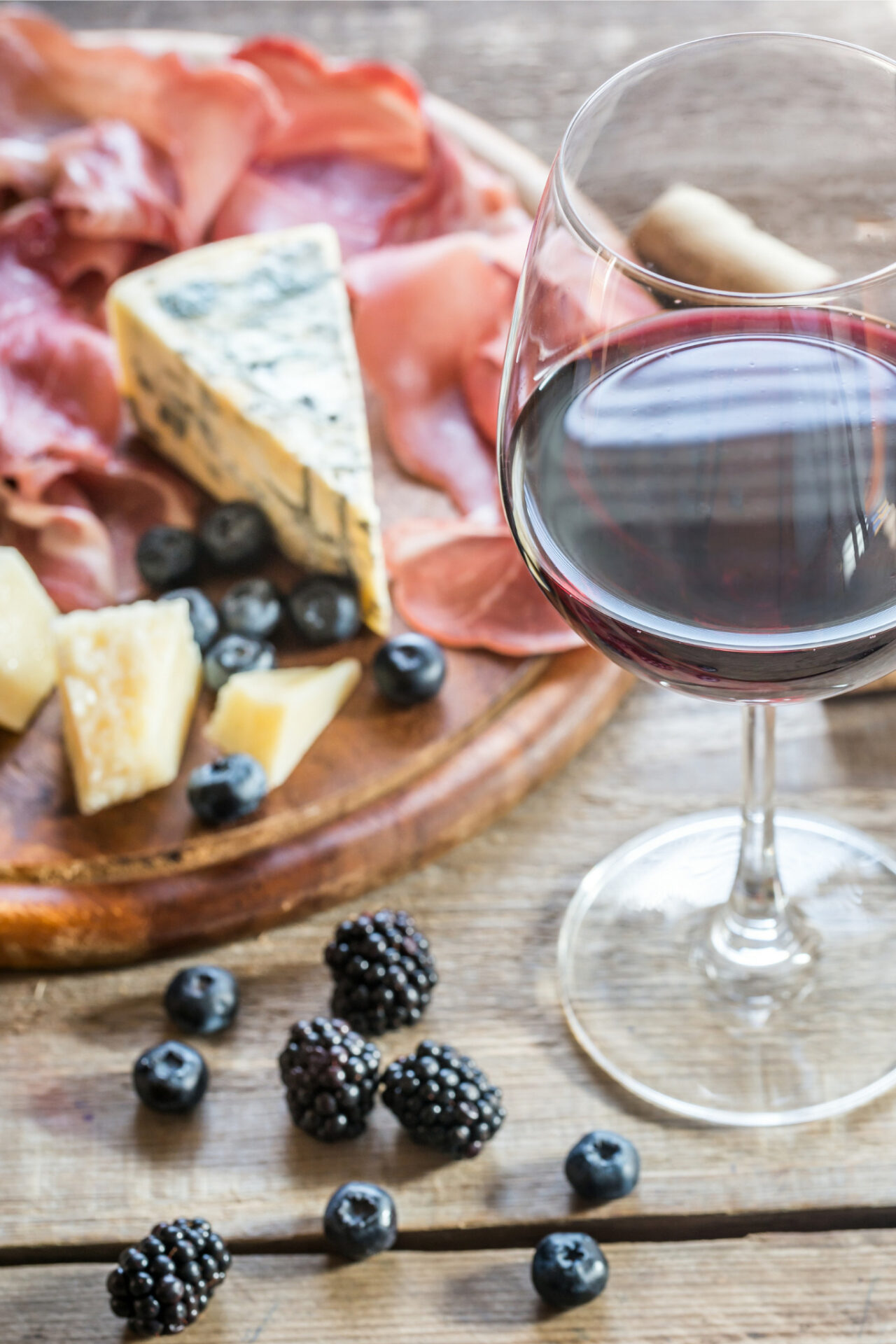 Syrah vs Shiraz Wine - red wine in a glass in front of cheeseboard with fruit
