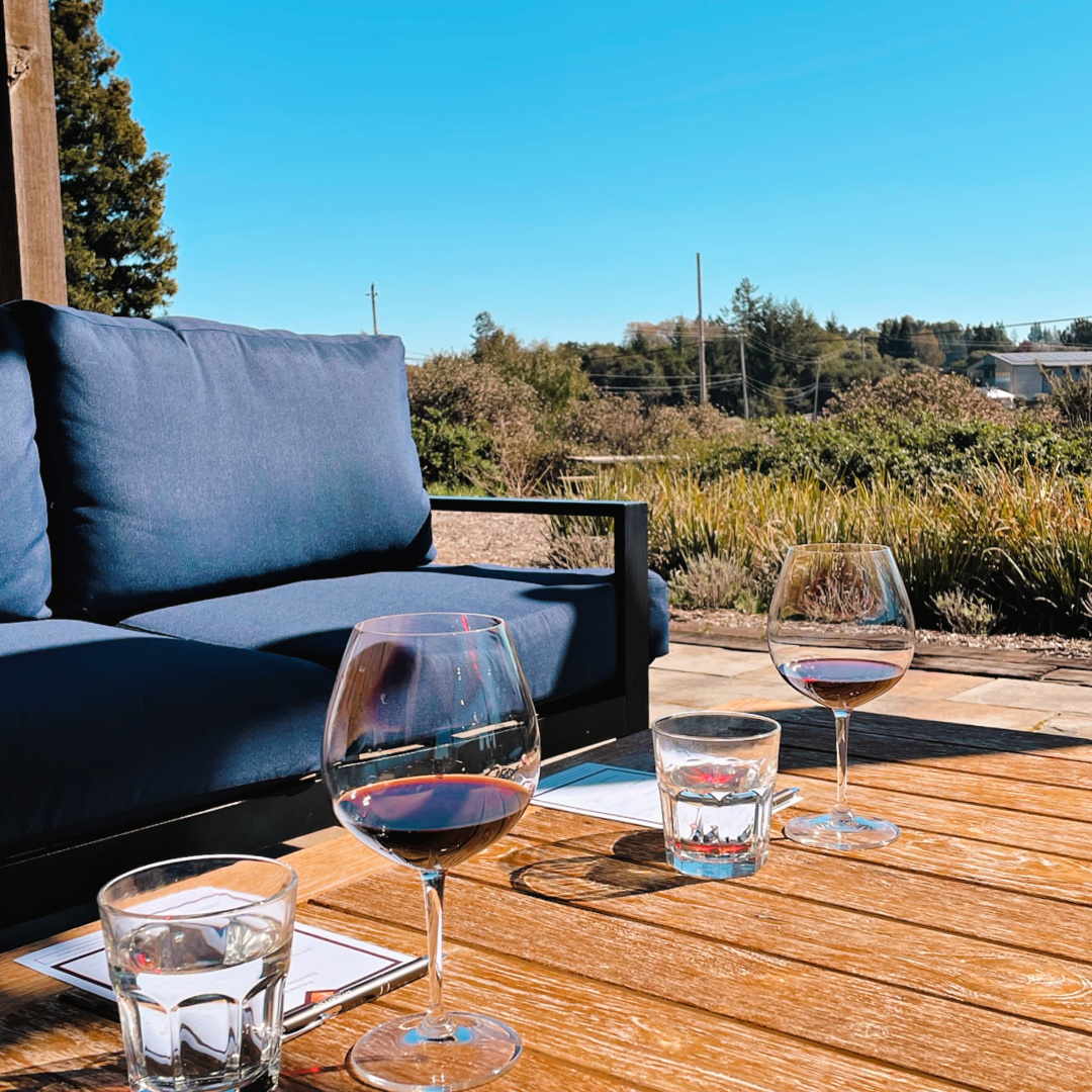 Two glasses of red wine sit on an outdoor table surrounded by patio furniture