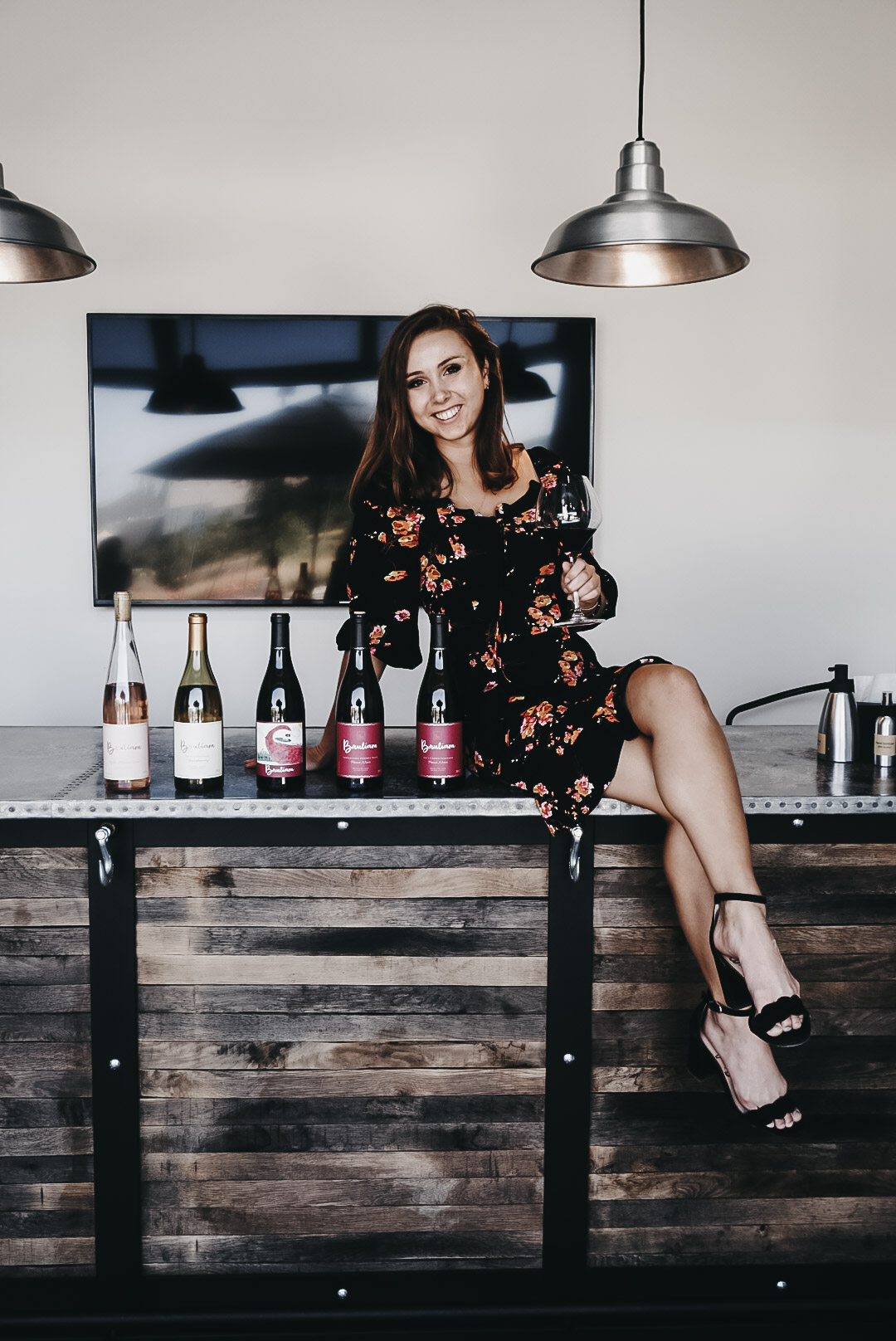 Paige sitting on top of a bar with an assortment of wine bottles from Bruliam