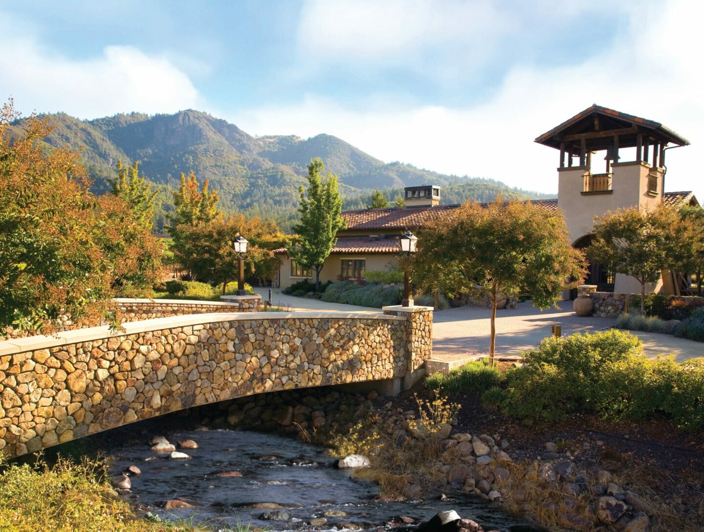 A bridge over a small brook, leading to a tower and a view of mountains looming in the background