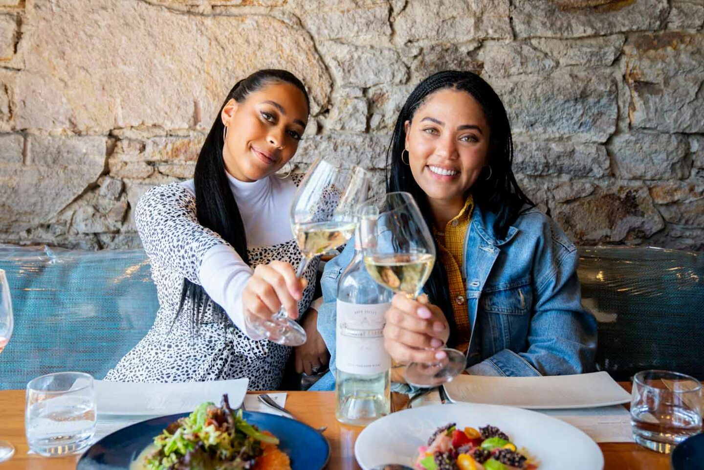 Ayesha and Sydel pose together, each holding classes of Domaine Curry Wine