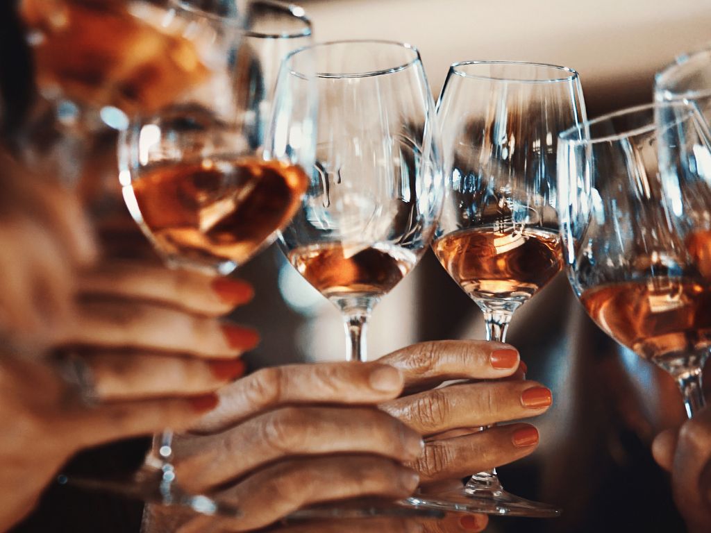 Group of hands cheersing with ice wine in stemmed wine glasses