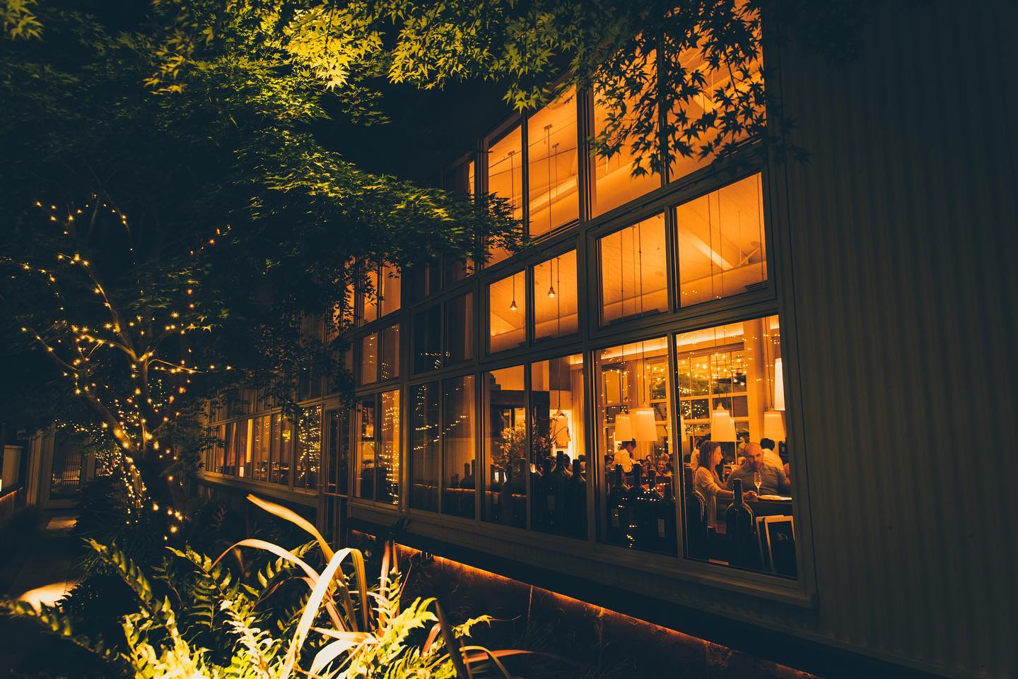 Exterior shot of PRESS Restaurant in St Helena, CA where restaurant goers can be seen enjoying dinner through the large glass windows