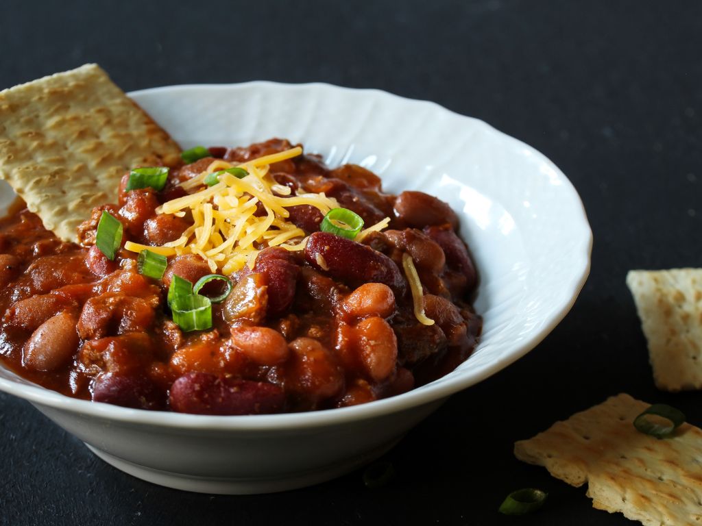 Vegetarian chili shown with cheese on top of bowl and cracker