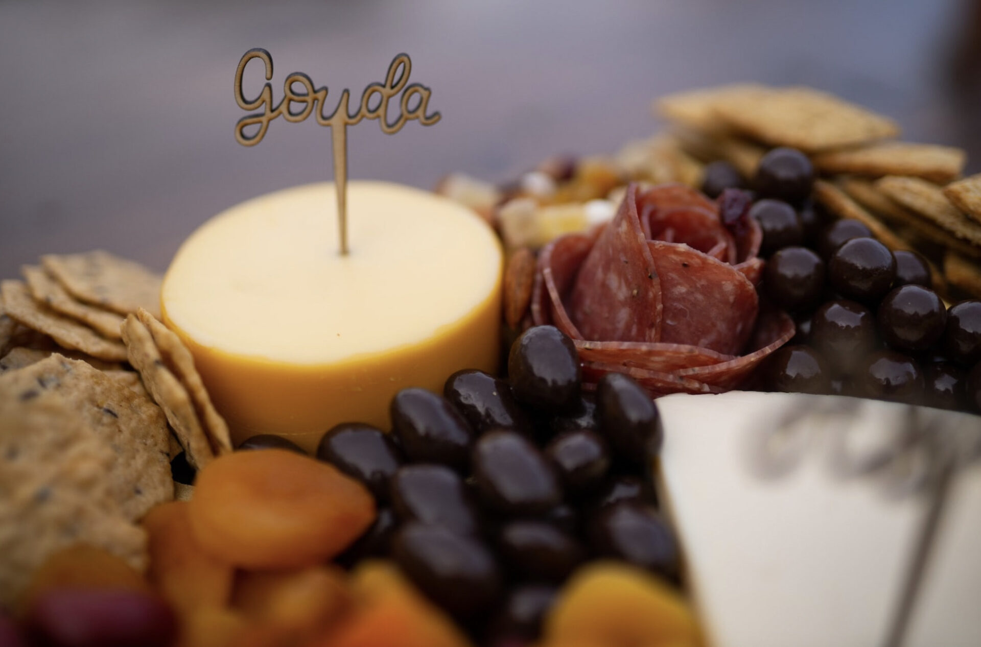 A charcuterie board with meats and gouda is marked with a small sign