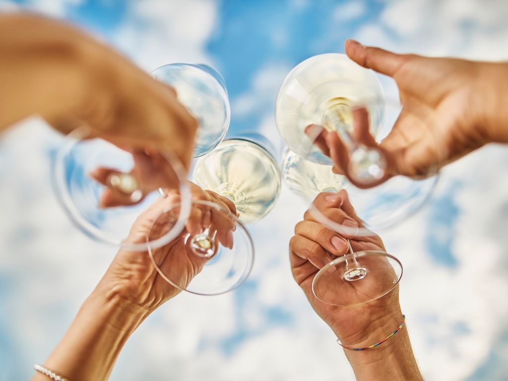 Is Pinot Grigio sweet? Four hands holding white wine glasses with the sky in the background