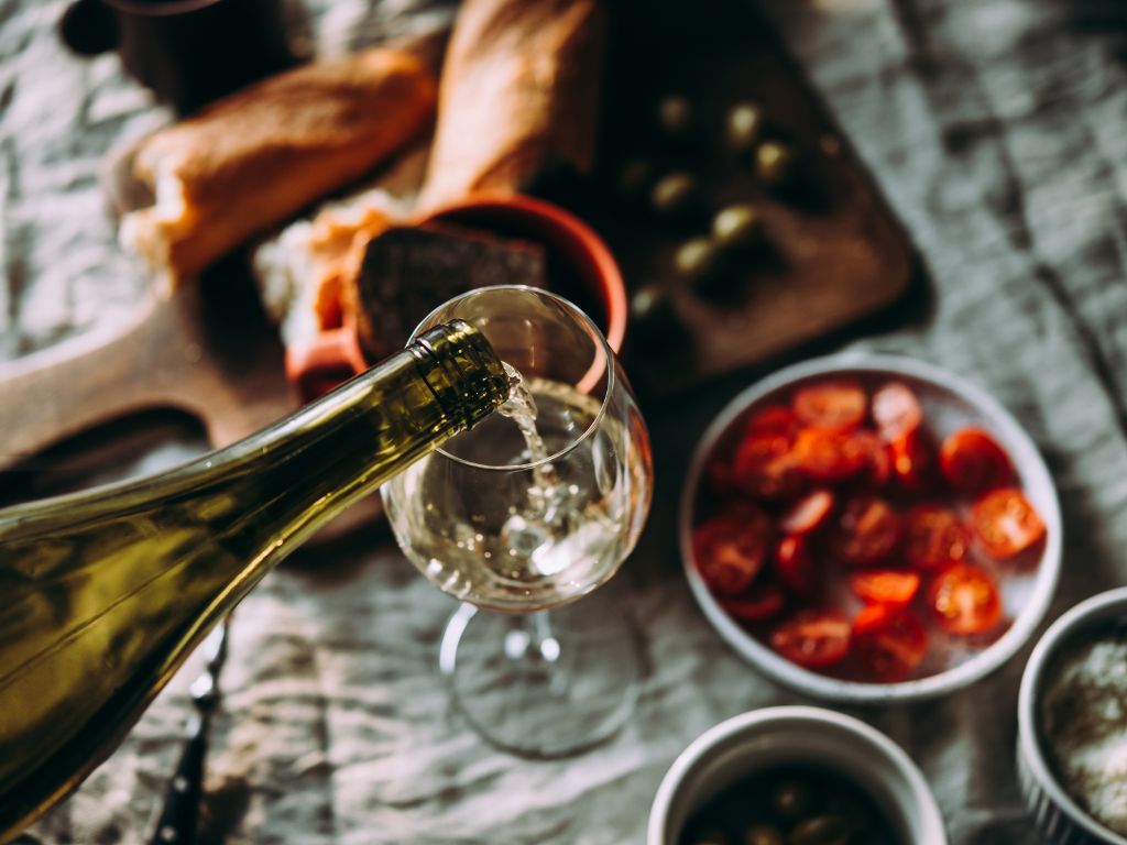 Italian white wine being poured in a wine glass over an assortment of Italian food