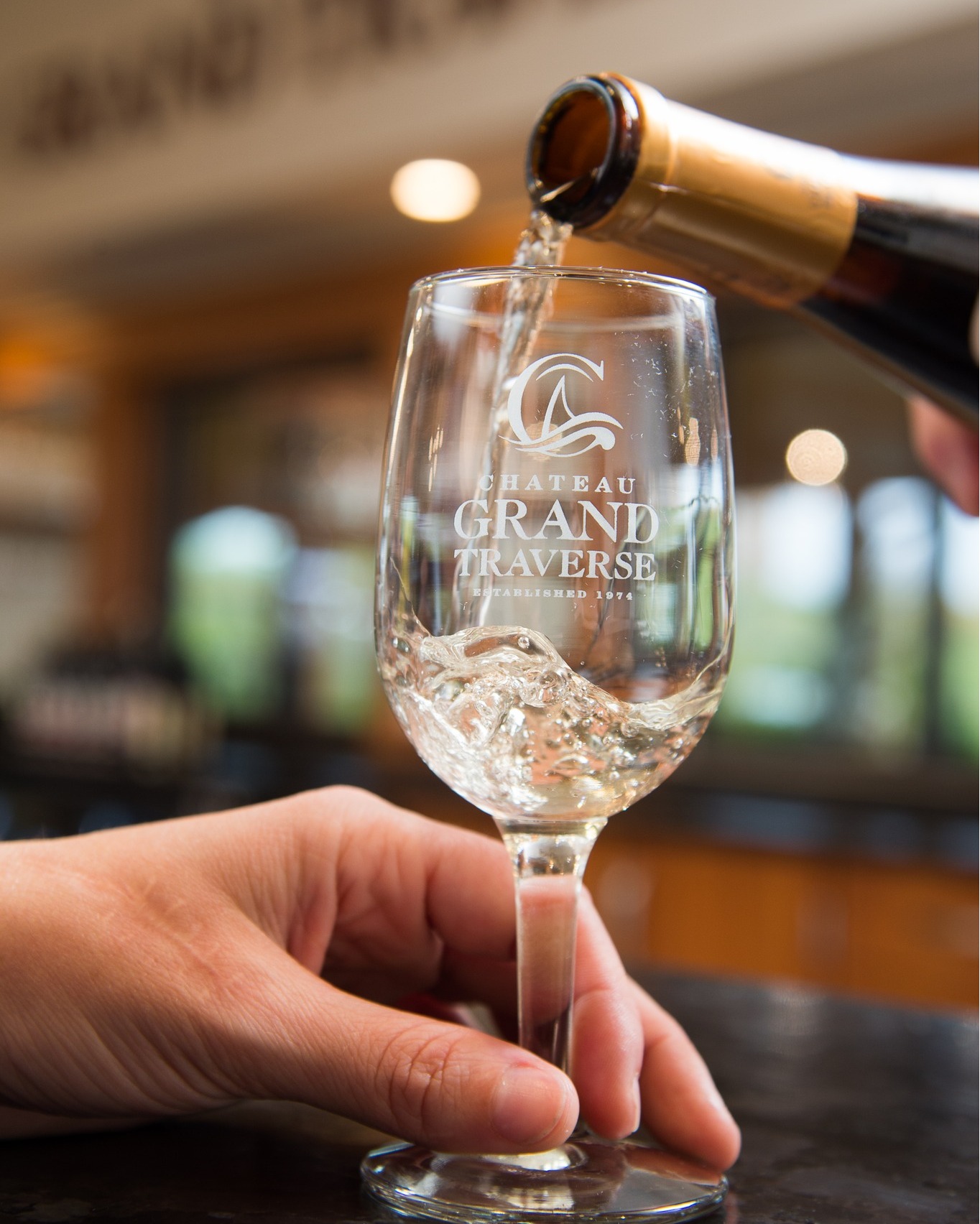 bottle of wine bringing pored into an empty glass, held by an expectant hand