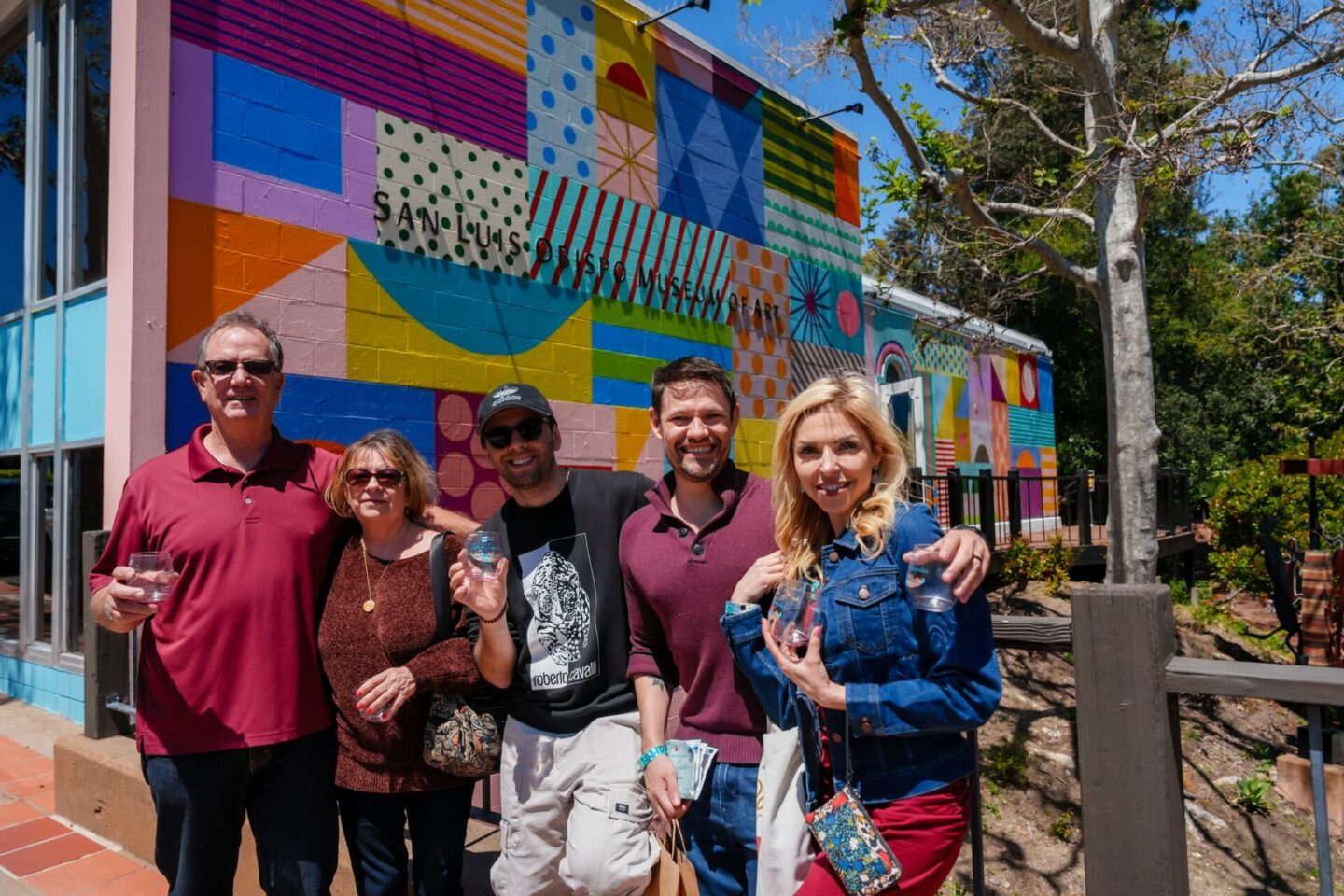 People pose for a picture by a mural in downtown SLO