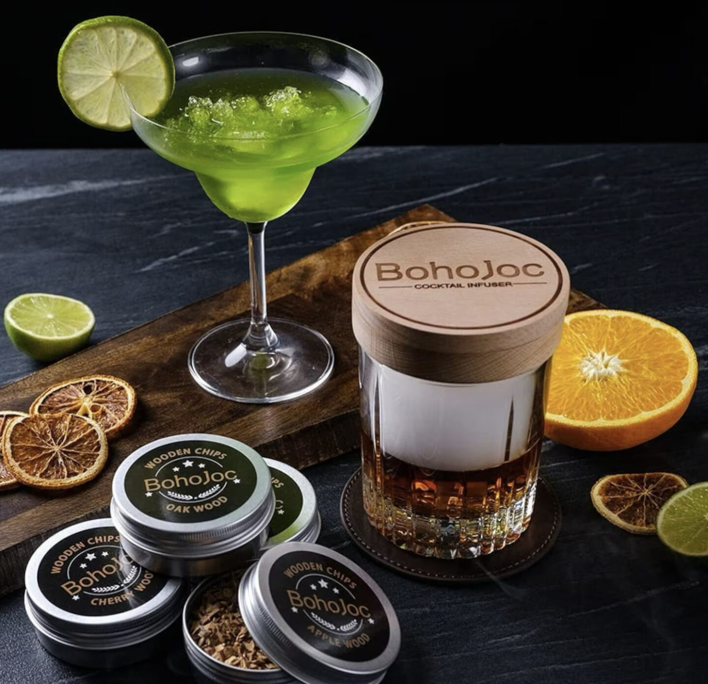 A cocktail smoker sits on top of a glass of whiskey, surrounded by wood chip samples