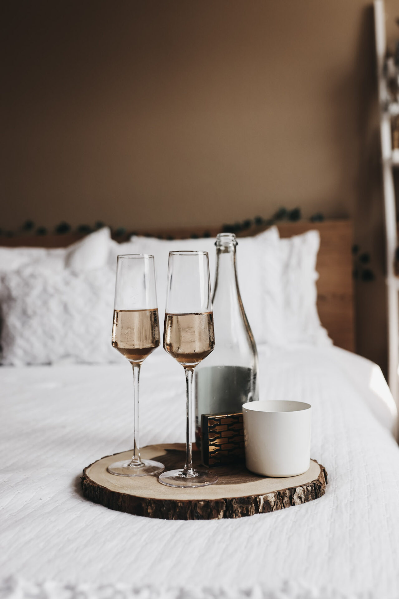 Blanc de blanc sparkling wine on a try with a wine bottle and candle on a white bed spread