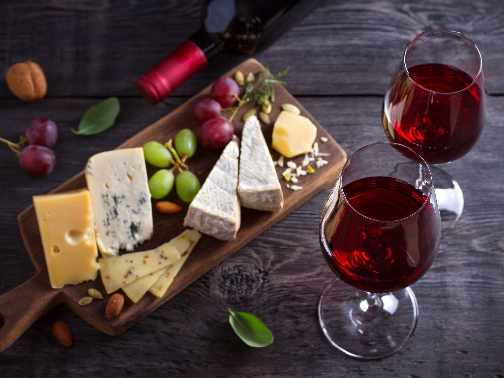 Two glasses of light red wine paired with various cheeses on a board