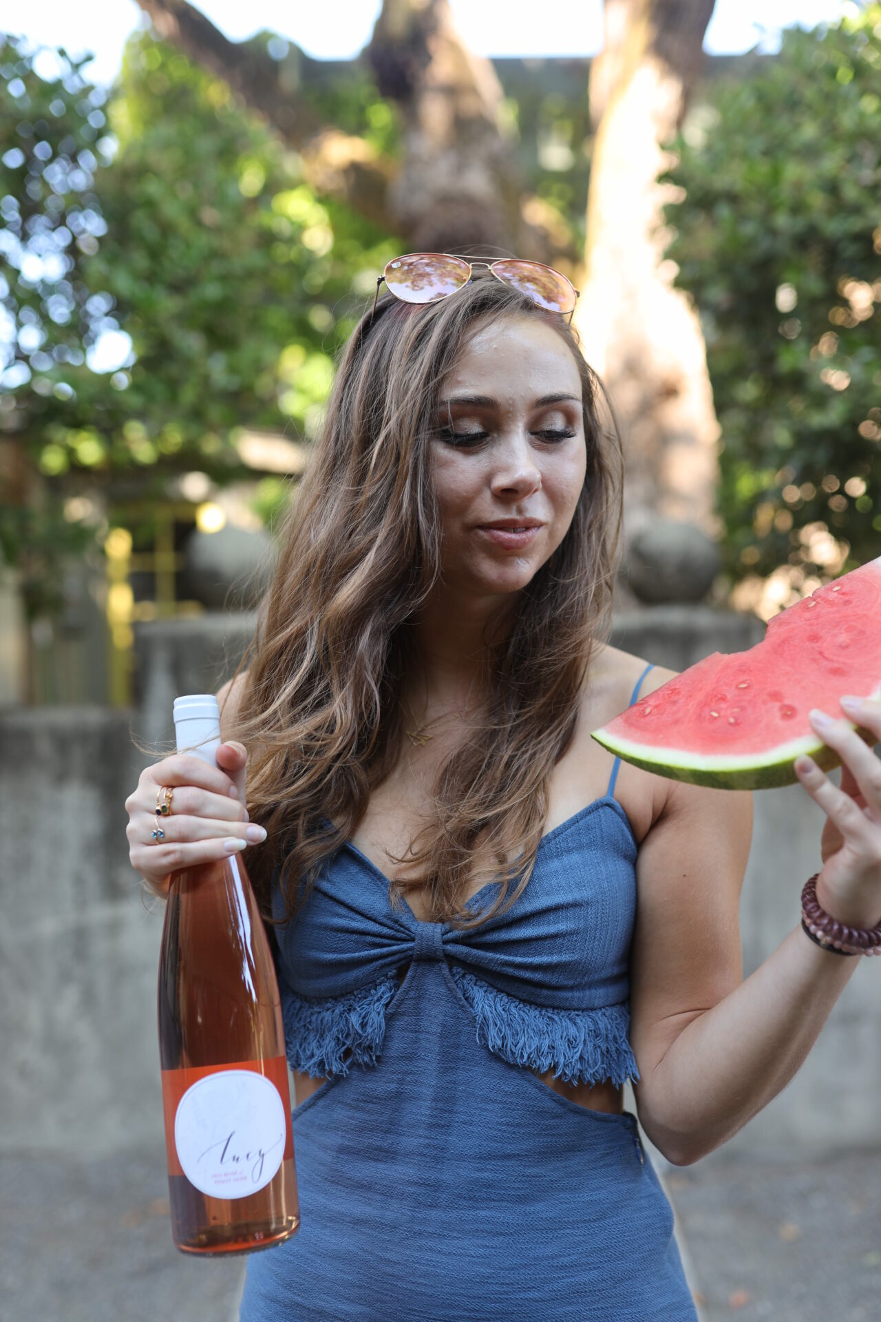 Paige eating watermelon and drinking rose outside during the summer in a blue dress