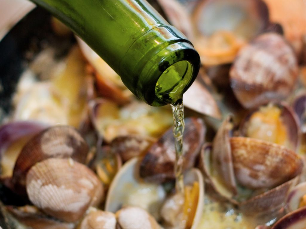 Dry white wine for cooking being poured into a seafood dish