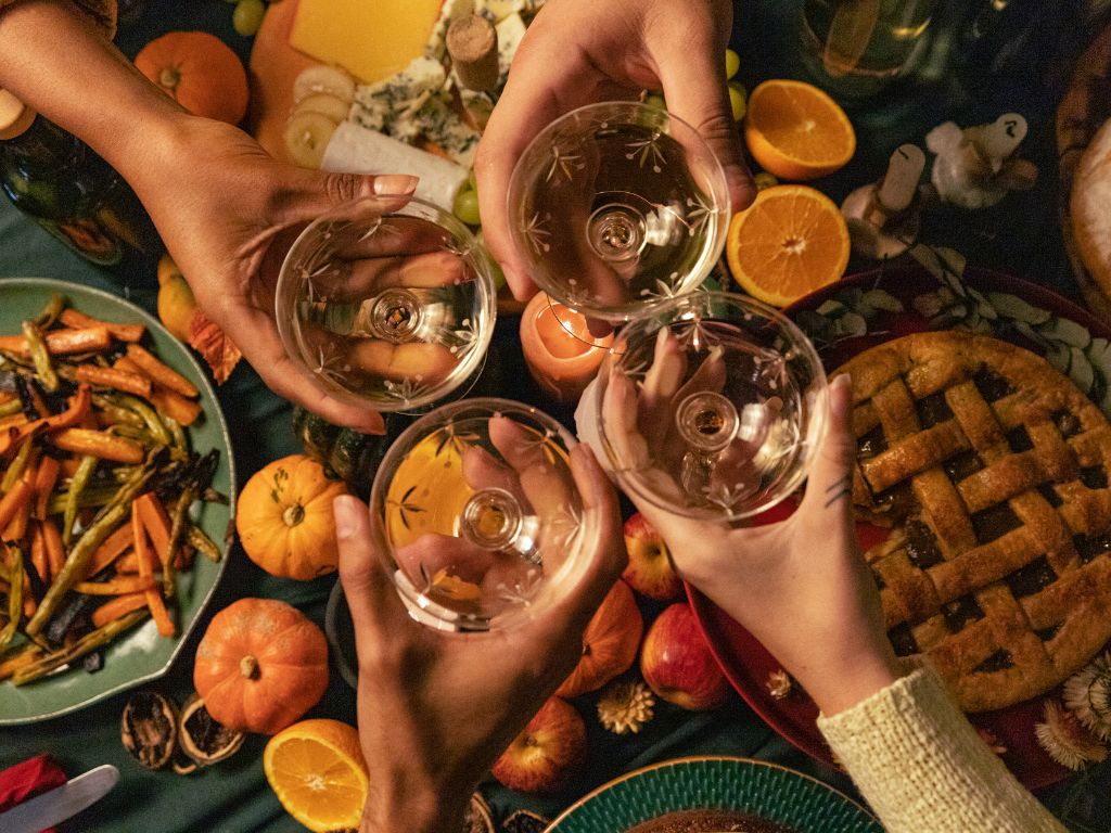 Four hands cheersing with white wine and turkey at thanskgiving dinner