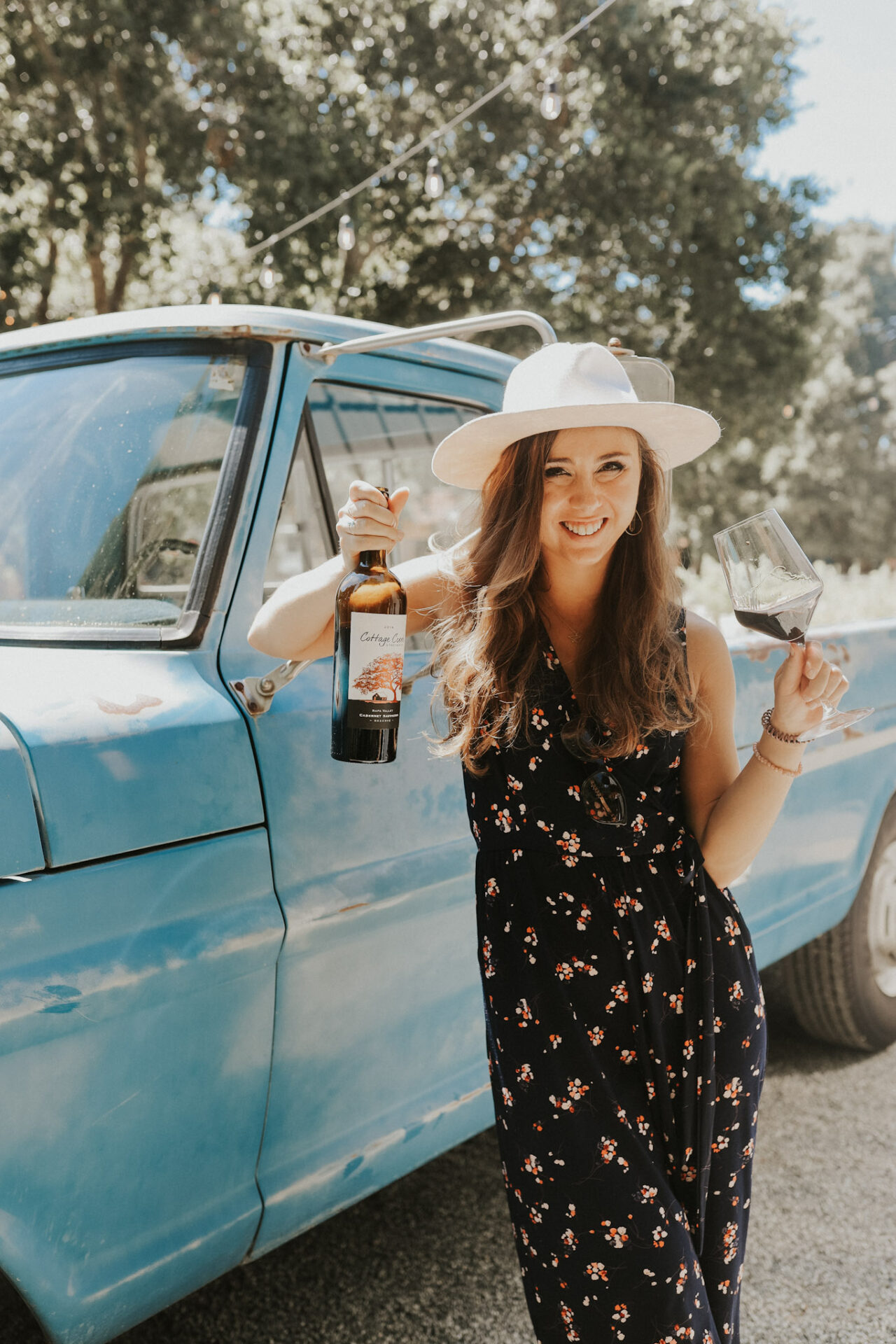 Paige leaning on a truck drinking a glass of dry merlot wine