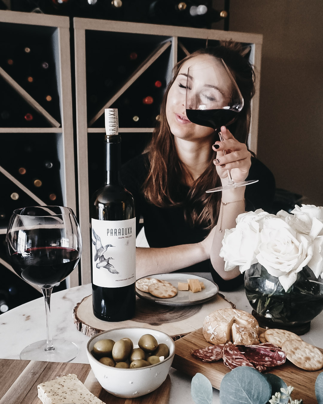 Merlot food pairings on a table with a woman drinking and a bouquet next to her