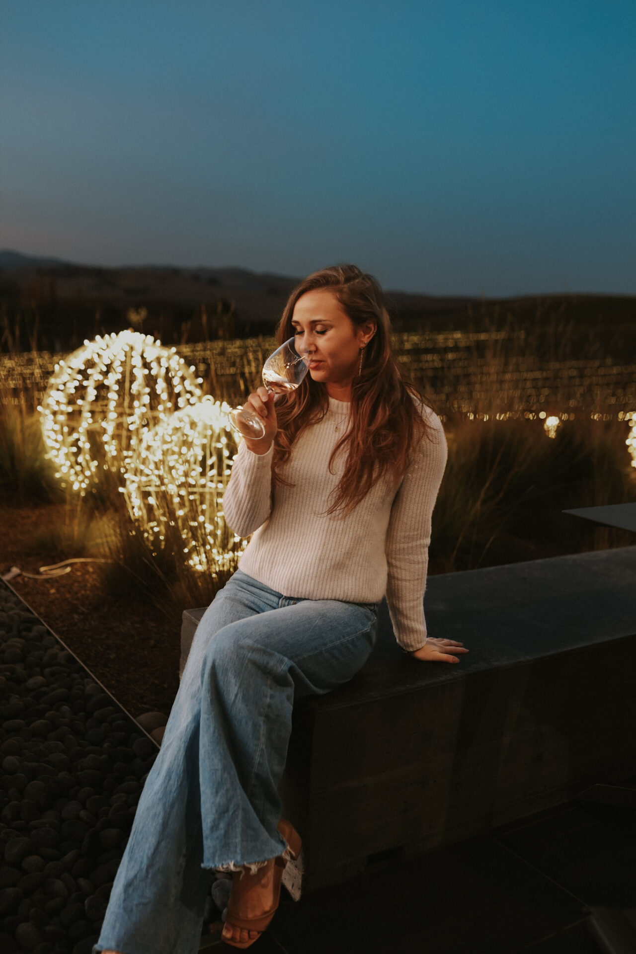 Paige with a glass of wine in front of holiday lights
