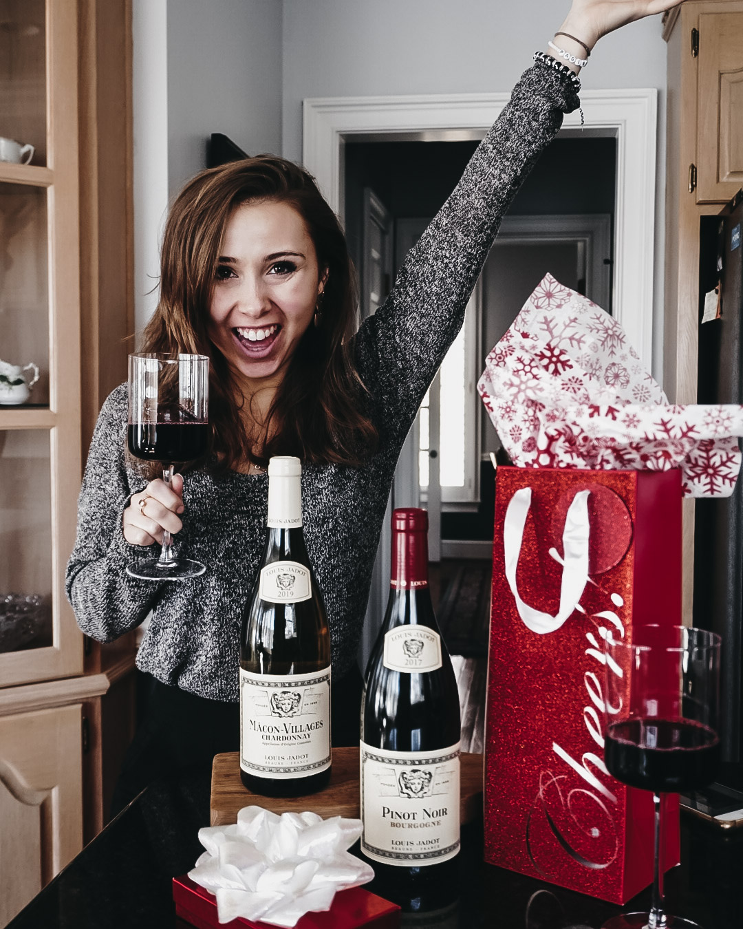 Paige holding wine and standing next to Holiday Wine Gifts for Winelovers in gift bags and boxes