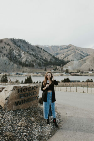 Paige at Rocky Pond estate winery in Orondo, WA next to sign with mountains in background