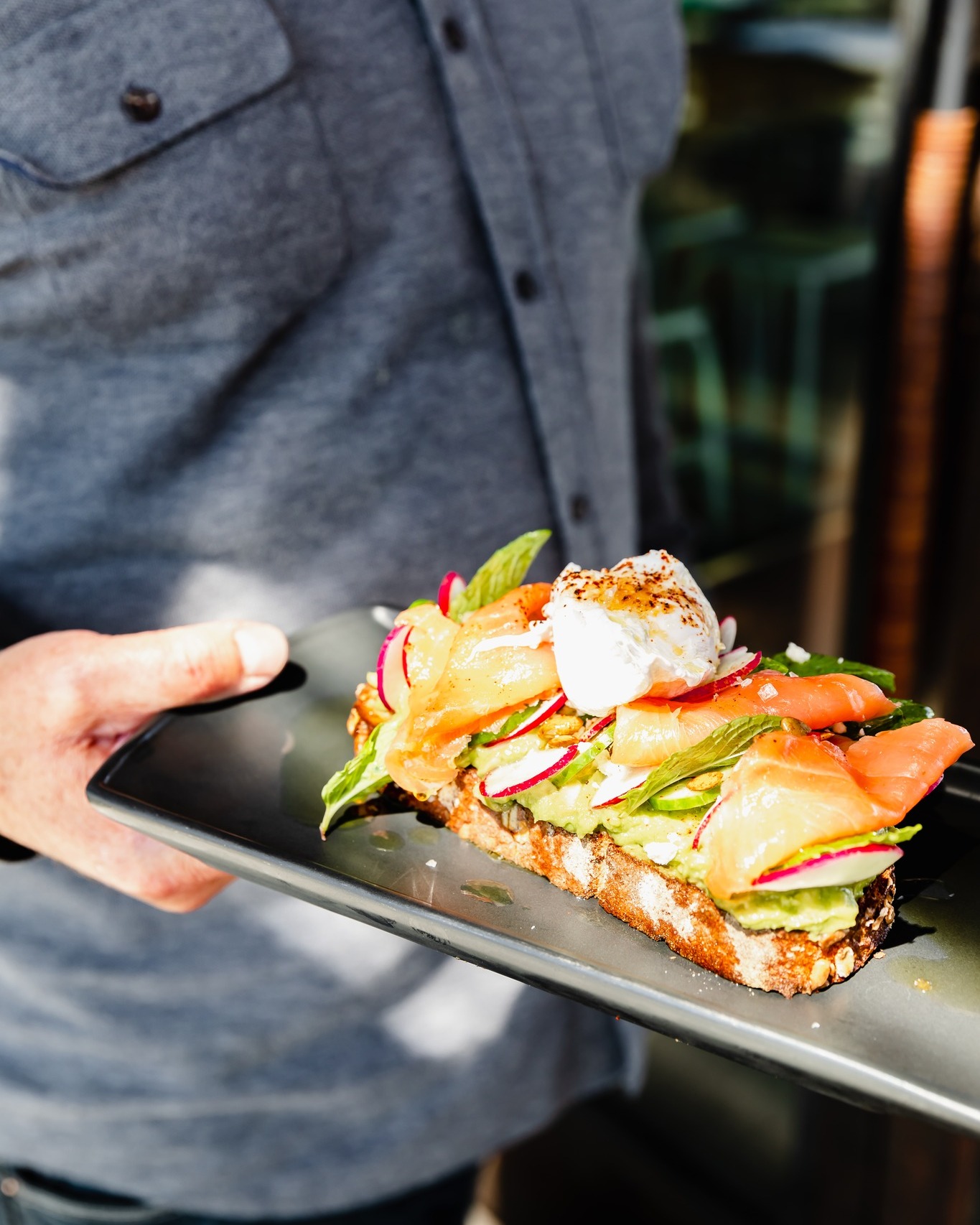 Hand holding a plate of avocado toast with smoked salmon