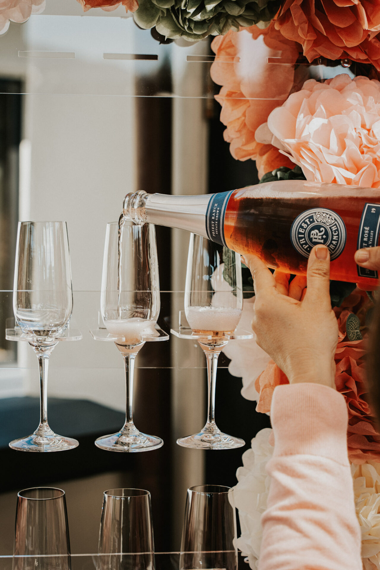 Priest Ranch sparkling rose wine being poured into flutes with flowers in the background