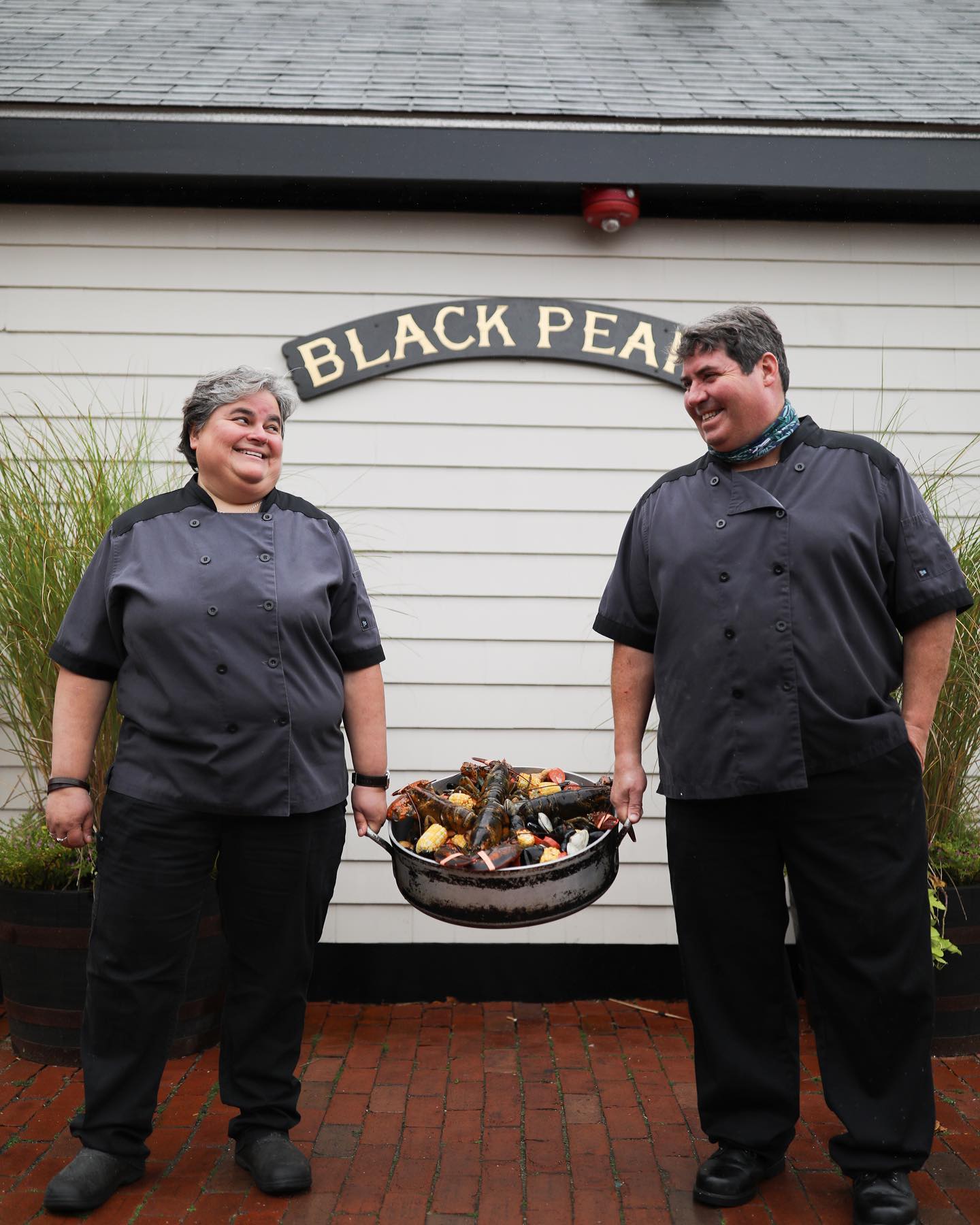 Two restaurants workers hold a basket of shellfish outside the black pearl