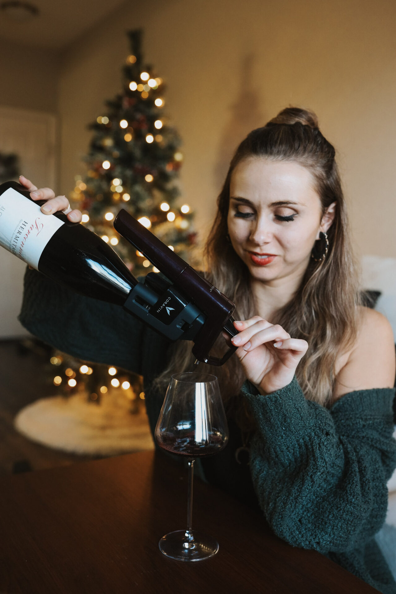 Paige with Coravin and bottle of wine in front of holiday tree