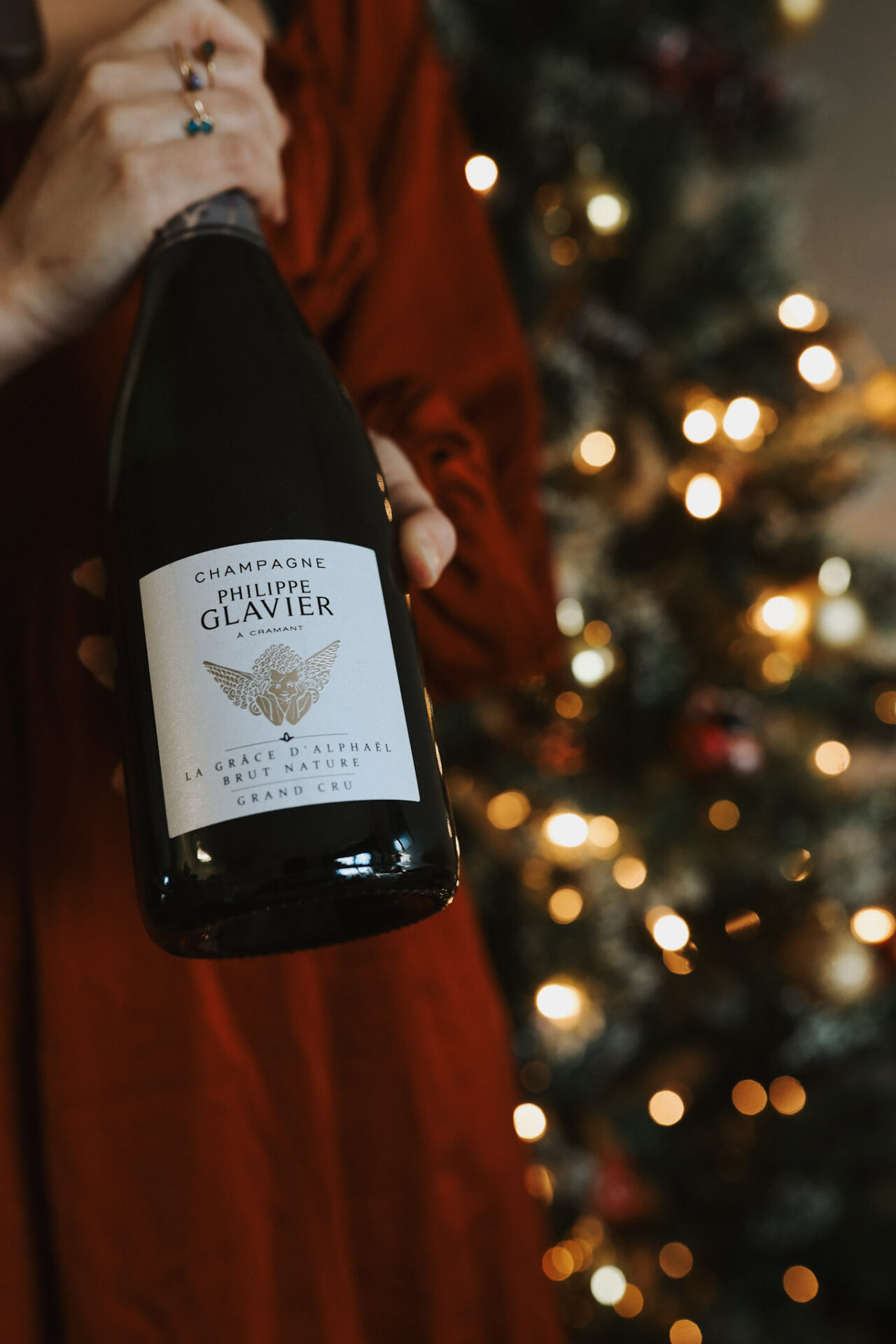 Hands with a bottle of champagne in front of christmas tree