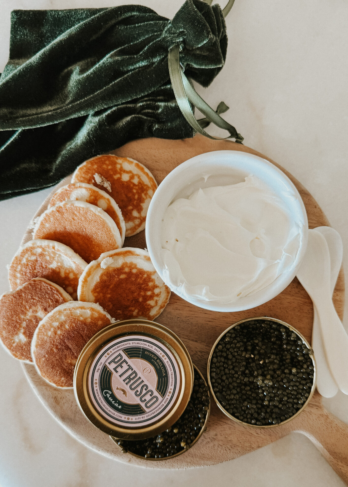 Petrusco Caviar tins on a charcuterie board with belinis, creme fraiche, and pearl spoons