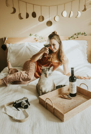 Malbec vs Merlot Wines - Paige on a white bed with red wine and her cat, Arwen. A camera is in the foreground