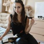 Paige on her bed with a glass of wine and two bottles wearing Vine & Vogue clothing rental